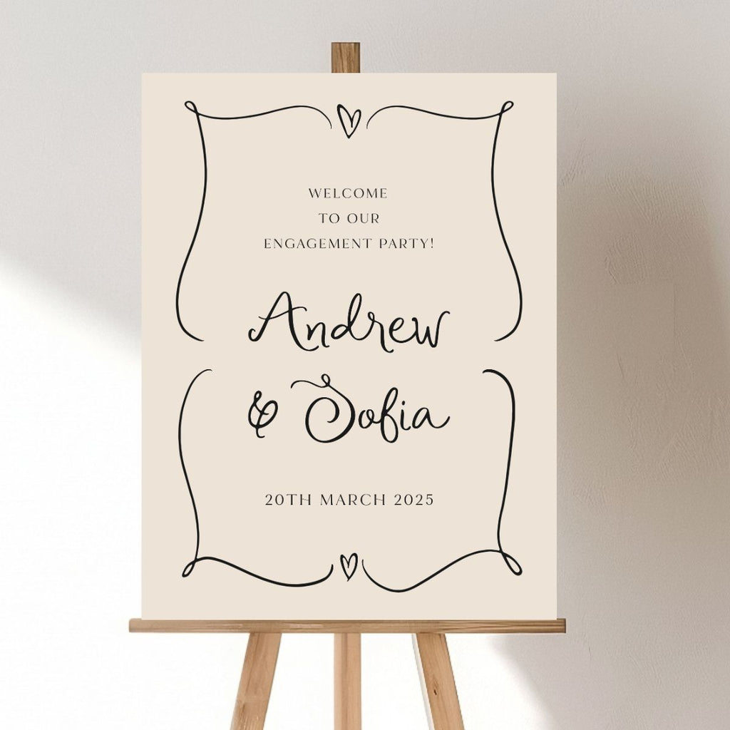 An easel holds the "Engagement Welcome Sign | Andrew & Sofia" by Etched Design, featuring a beige background with personalized, elegant cursive writing. The sign is adorned with delicate corner flourishes and small heart accents. The text reads, "Welcome to our engagement party! Andrew & Sofia. 20th March 2025." The softly lit background wall enhances the minimalist charm of this beautifully crafted piece.