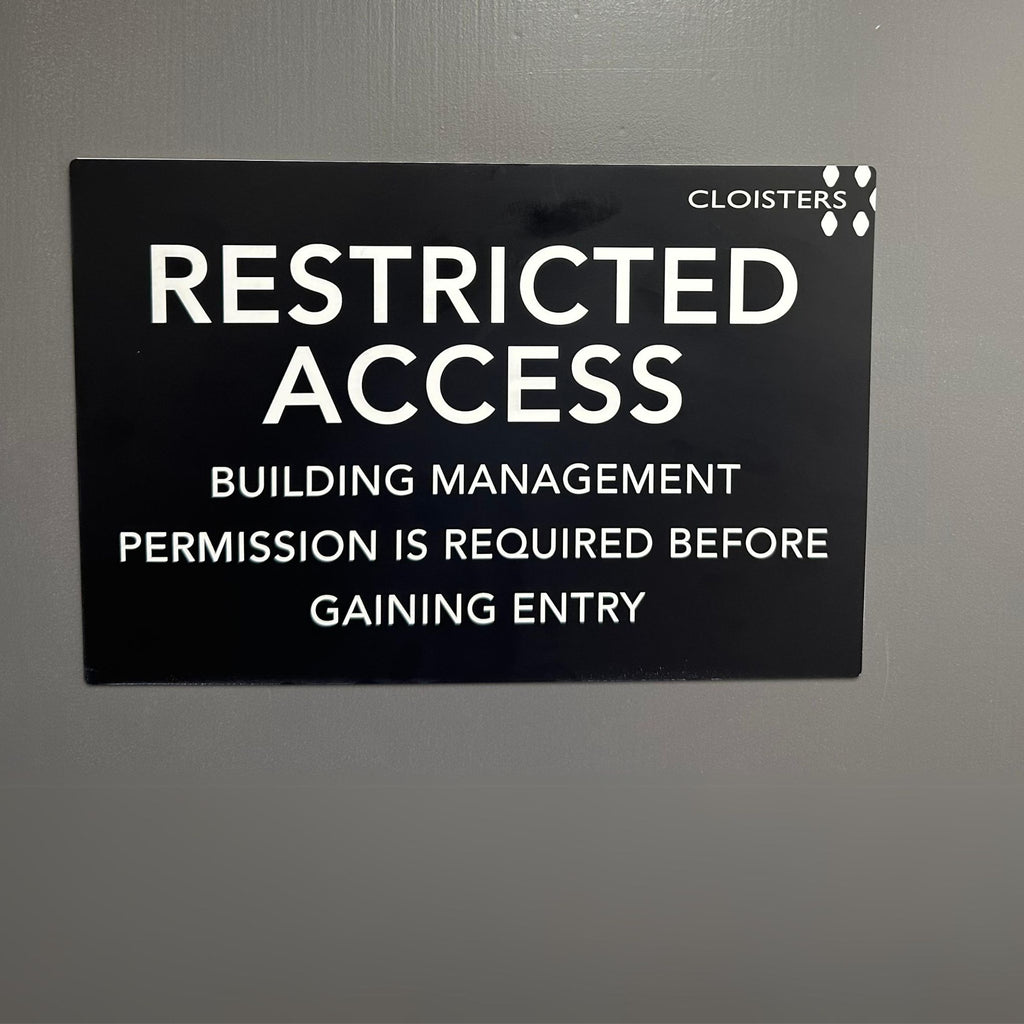 A black sign with white text on a gray wall reads: "Cloisters Restricted Access. Building management permission is required before gaining entry." The custom-designed Acrylic Business Sign by Etched Design, made from durable Traffolyte, ensures durability and clarity.