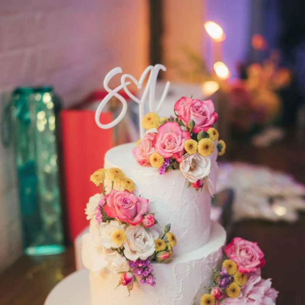 Initial white wedding cake topper with heart.  Three layered white buttercream cake with fresh spring flowers.