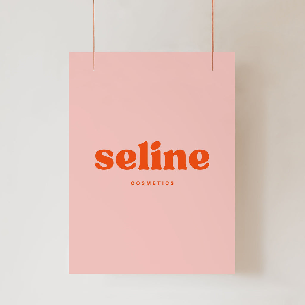 A UV-resistant poster from Etched Design, featuring the word "seLine" in bold, red uppercase letters at the center. Below it, "COSMETICS" is written in smaller uppercase red letters. The precision of digital printing ensures high quality. The pink UV Printed Business Sign hangs by two strings from the top corners against a light-colored background.