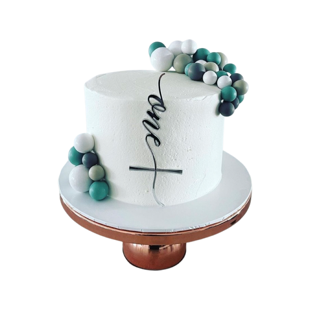 The Cake Fropper | Single Layer from Etched Design is a white frosted cake with a minimalist appearance, elegantly displayed on a copper stand. It features spherical fondant or gum paste balls in hues of green, grey, and white that cluster at the top and side. The front showcases the calligraphic word "one" piped in black icing, accompanied by a custom acrylic cake plaque.