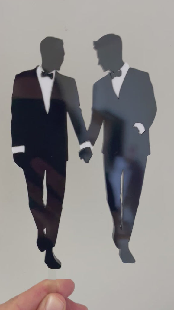 Gay couple in black and white tuxedo holding hands cake topper