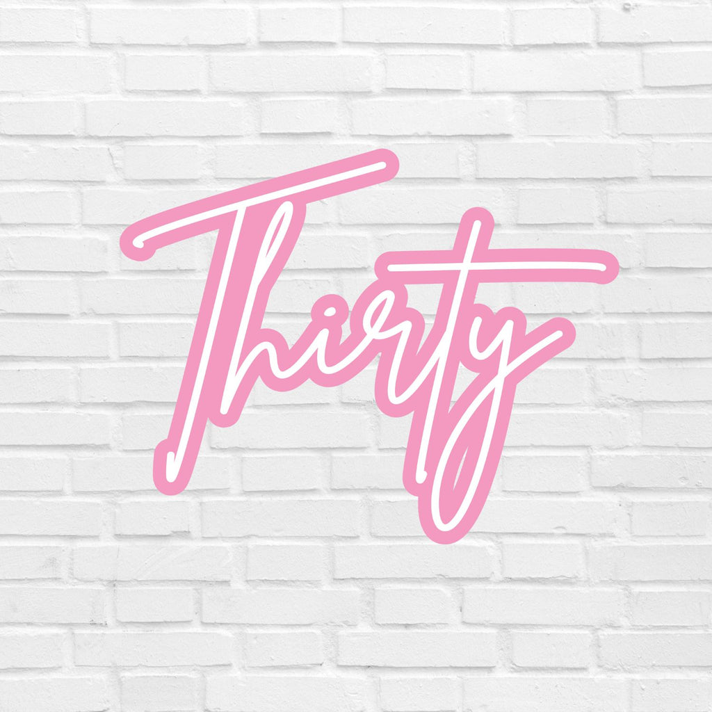 A white brick wall serves as the backdrop for the "Name Plaque | 3D" by Etched Design, showcasing the word "Thirty" written in a bold, cursive pink font with a 3D appearance.