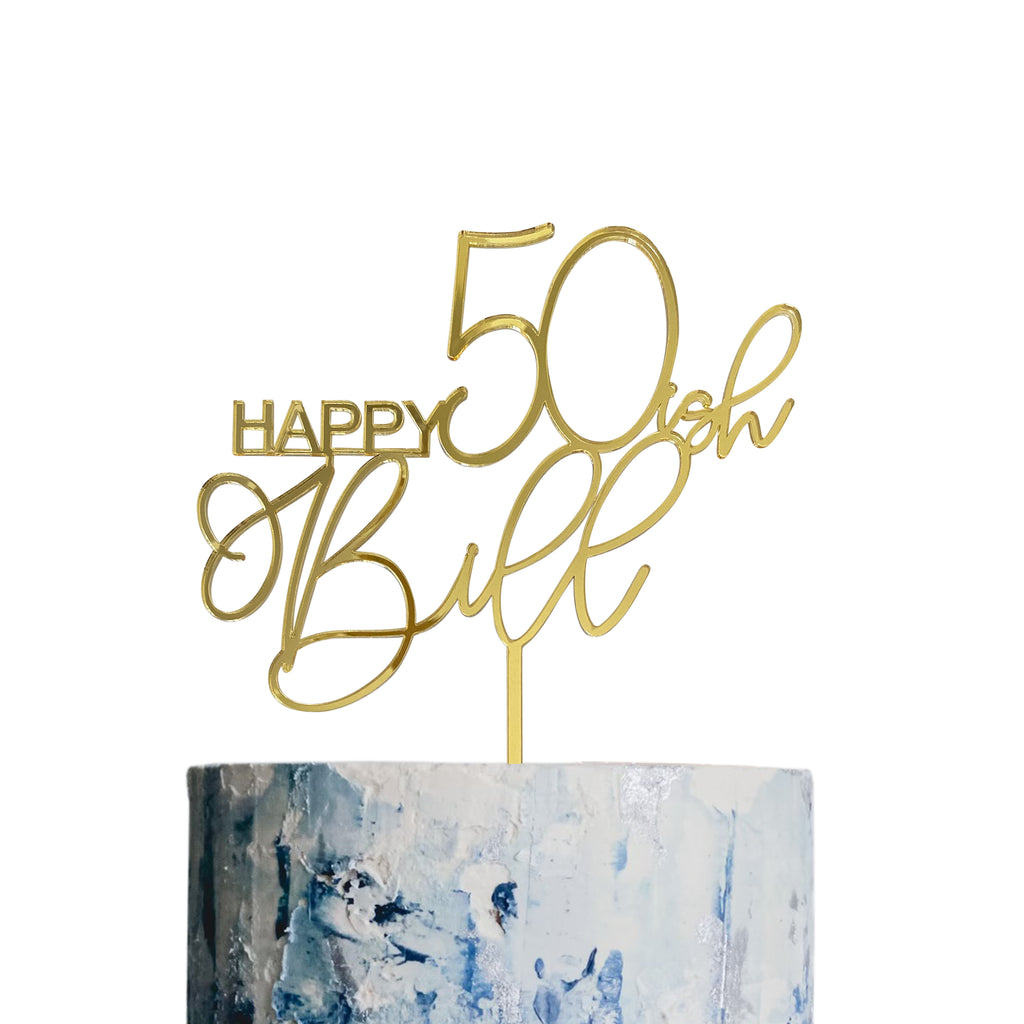 A Script Birthday Cake Topper from Etched Design with gold cursive text reads "Happy 50ish Bitth." The perfect personalized touch sits atop a white and blue marbled birthday cake, which is just partially visible at the bottom of the image. The background is plain white.